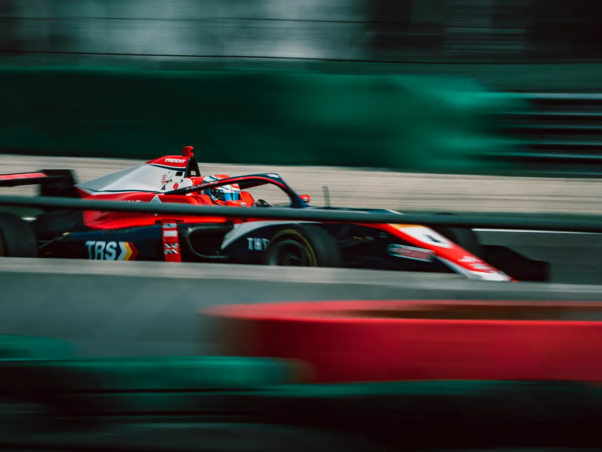 Un monoplaza de carreras a alta velocidad en un circuito, con el fondo en movimiento